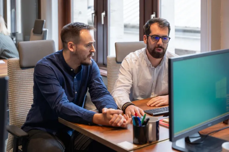 Two offshore developers working together at a computer workstation, reviewing software projects and collaborating on application development in a modern office environment.
